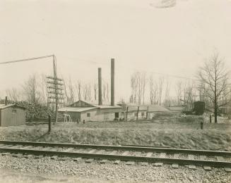 A photo of an industrial building or factory with two smokestacks and beside some railway track ...