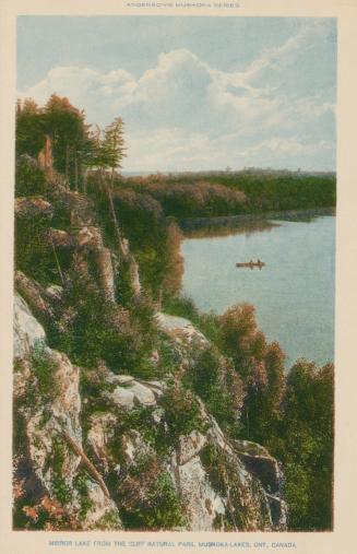 A tree covered cliff with two people in a canoe on a lake in the background.
