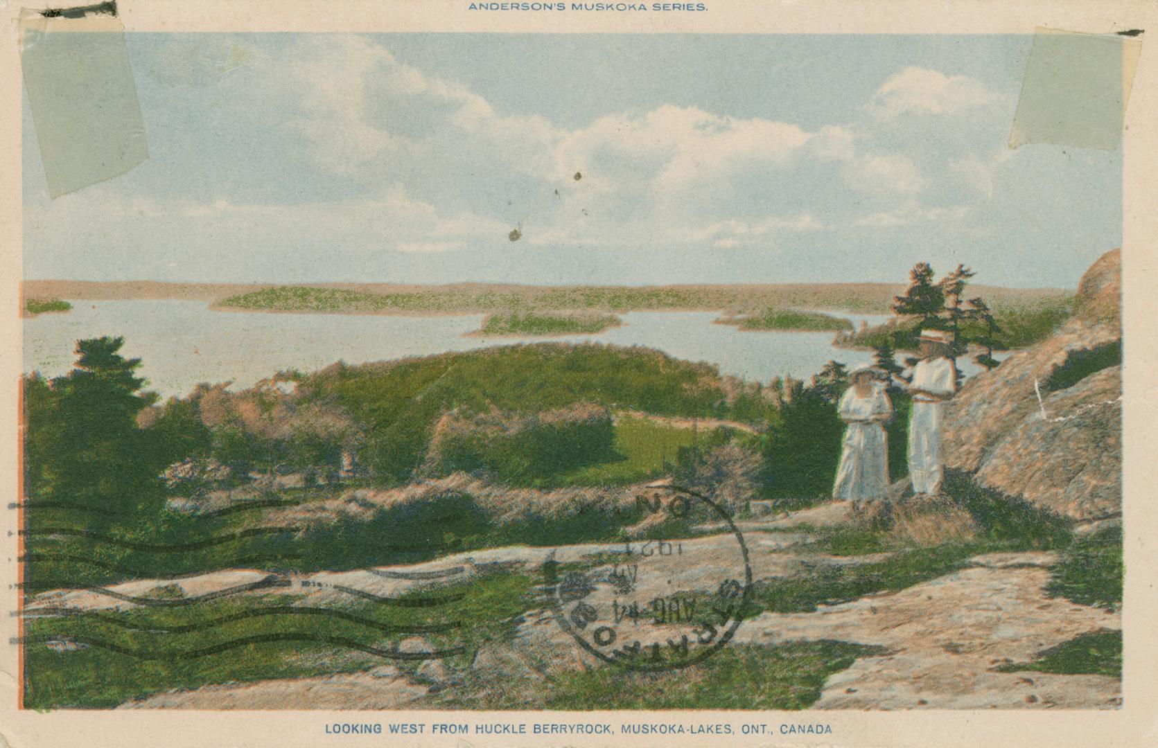 A man and a woman standing on a rock surface looking out over a vista of trees and lake.