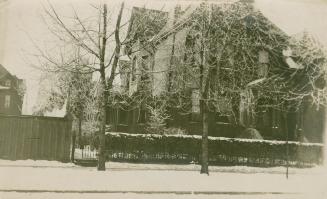 Picture of a large three storey brick house with trees out front. 