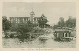 Black and white picture of a three story hotel complex on the shore of a lake.