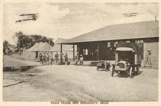 Sepia toned picture of men standing in from of a one story commercial building with two planes …