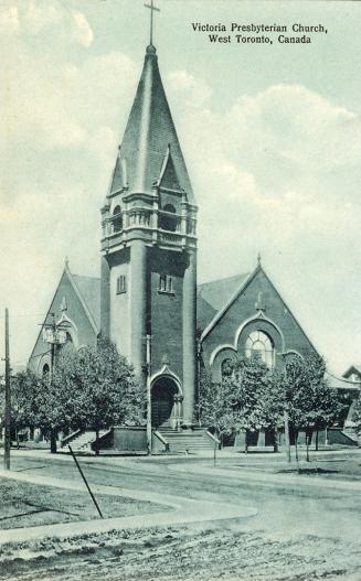 Picture of large church with tower on street corner surrounded by trees. 