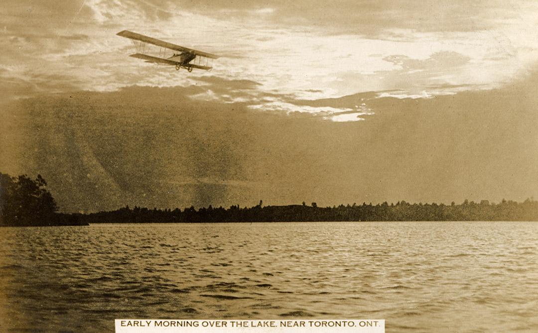 Black and white shot of an air plane flying across a body of water.
