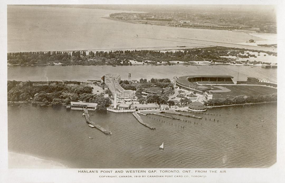 Aerial shot of houses and an amusement park on land beside a lake. B & W.