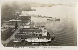Aerial shot of a large city harbor with ships and boats, beside a lake. B & W.