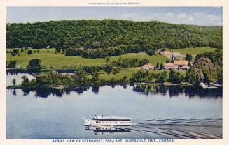 A steamship on open water in from of wooded land and a hotel complex.