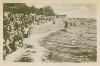 Black and white picture of a crowd of people splashing the water beside a sandy beach.