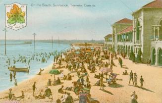 Colorized photograph of a crowd of people on a beach with large buildings to the right.