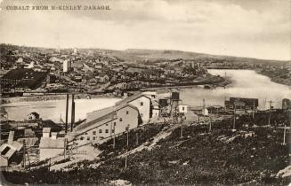 Black and white photograph of mining buildings beside a lake.