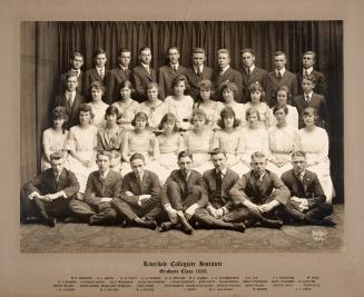 A photograph of thirty-seven students posing for a class photo in front of a set of curtains. A…