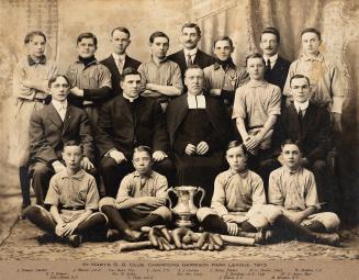 A photograph of a baseball team posing with bats, gloves, a ball and a trophy in a photo studio ...