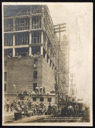 A photograph of a large group of construction workers posing in front of a partially-built eigh ...