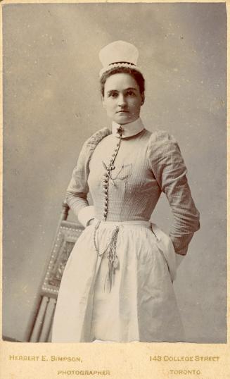A posed photograph of a young woman wearing a nurse's uniform. She is standing in front of a ro ...