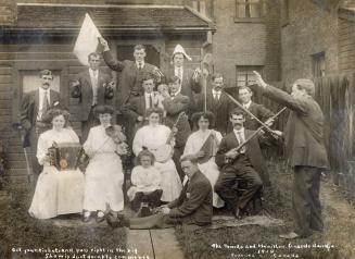 A photograph of a group of men and women, and one young girl, posing in front of a building and…