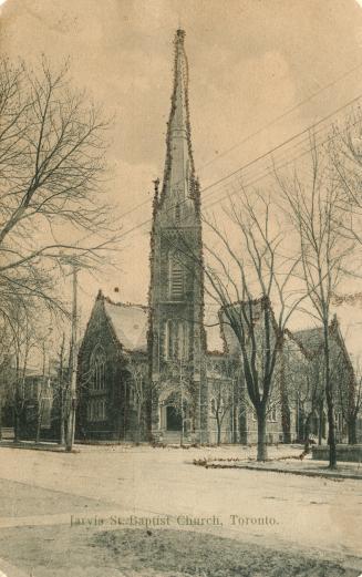 Picture of large stone church on street corner with prominent steeple and trees surrounding it. ...