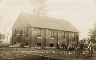 Picture of one storey church building with people standing out the side. 