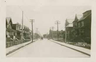 Black and white photograph of a horse and buggy driving down a street with houses on either sid…