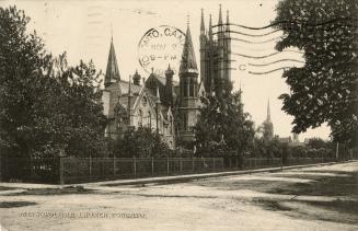 Street view of cathedral church surrounded by iron fence and trees. 