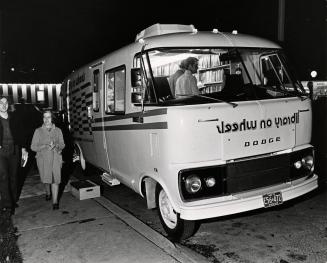 Two people walk past a parked bookmobile on a dark evening. 