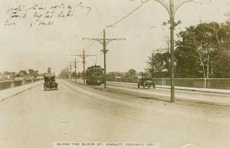 Black and white photograph of a street car and automobiles driving across a bridge.