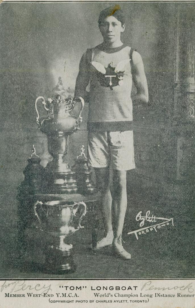 Black and white photograph of a young man in athletic gear standing beside four trophies.