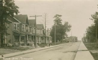 Black and white photograph of a street with two story houses on one side.