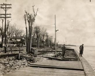 Picture of two men standing on section of washed out lake boardwalk with houses on left. 