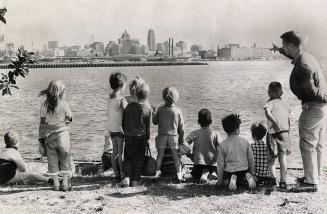 Picture of a group of children and adult looking out over lake to city skyline. 