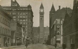 Black and white photograph of a Richardsonian Romanesque building with a clock tower at the end ...