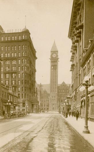 Sepia toned photograph of a busy city street with a large public building with a clock tower at ...