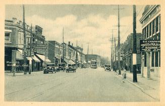 Black and white photograph of a city street. Cars and a street car on the road.