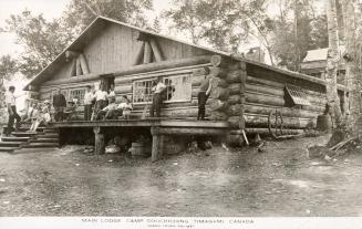 Black and white photograph of a group of men standing on the verandah of a log cabin.