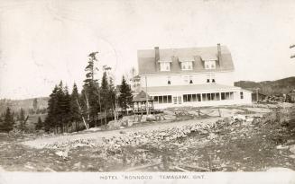 Black and white photograph of a hotel in a wild, wooded area. 
