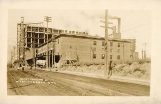 Black and white photograph of a factory building with street car tracks in front of it.