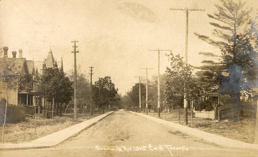 Black and white photograph of houses on a tree-lined street.