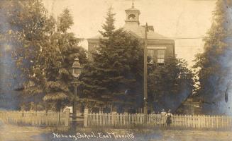 Black and white photograph of two girls standing in front of fence in front a collegiate buildi…