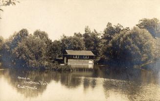Black and white photograph of a small building by the side of a pond.