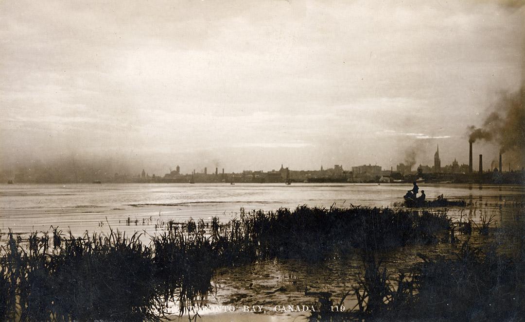 Black and white photograph of a city seen in a distance across a body of water.