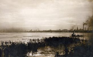 Black and white photograph of a city seen in a distance across a body of water.