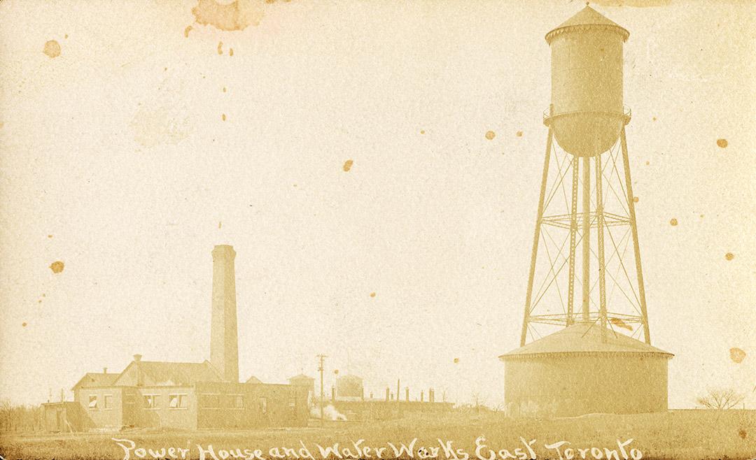 Black and white photograph of a large, water tower in front of an industrial building.