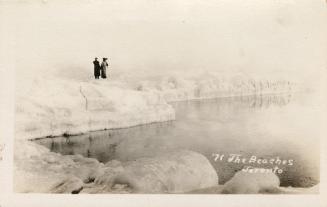 Picture of two people standing on ice formations at the edge of water. 