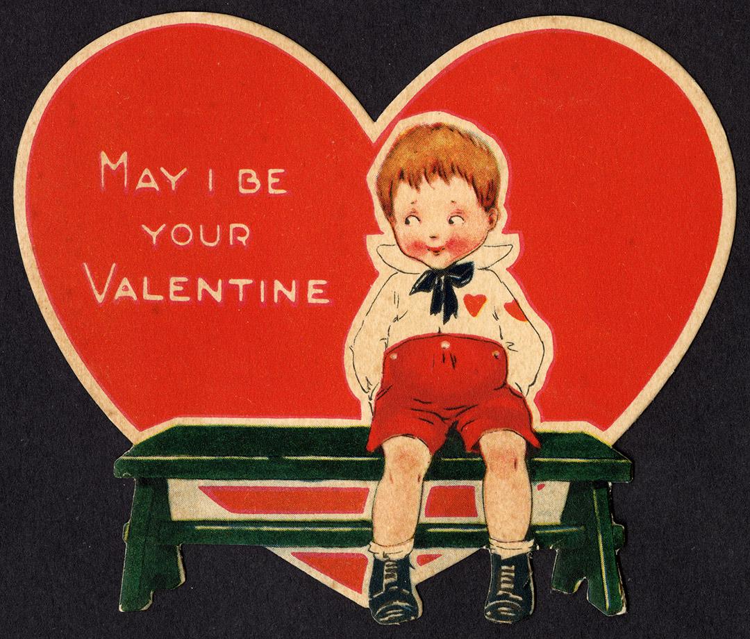A red heart shaped card. It pictures a boy sitting alone on a bench. He is looking off to the s…