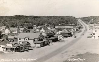 Black and white photograph of a highway going through a small town in the wilderness.