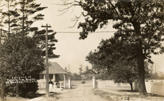 Black and white picture of open gates with a road leading into a large area with house in it.