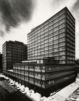 A photograph of a large split-level office building, located at the corner of a city street. Th ...