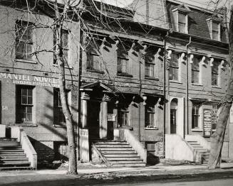 A photograph of a row of three-story townhouses, with stairs leading to the front door of each  ...
