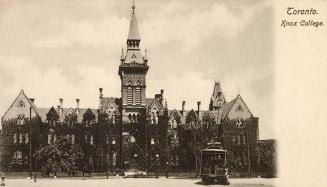 Black and white photograph of a gothic school building with a central tower. Streetcar in the f ...