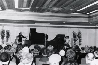 Two women play on two pianos for an audience. 