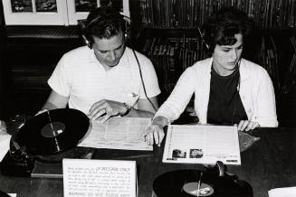 Two people sit at a desk listening to records in a music library. 